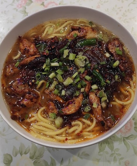 Bowl of Tibetan Thukpa topped with fried spicy mix in a white bowl on a table.