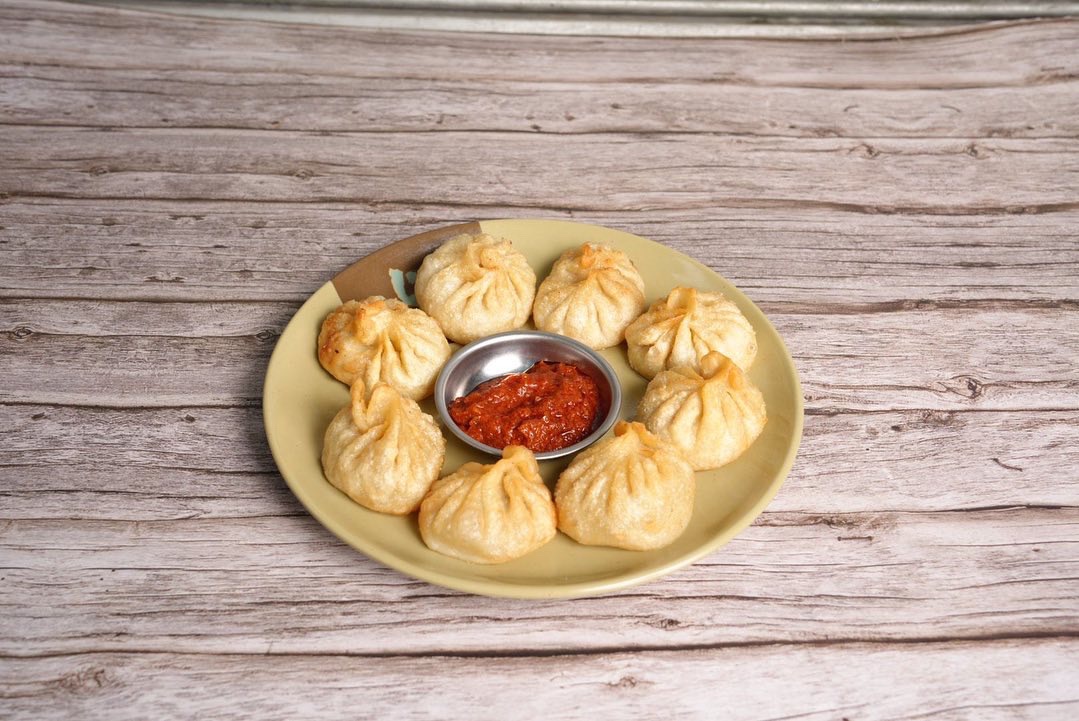 Tibetan Momo chicken dumplings with a spicy red sauce, served on a white plate against a dark wood table background.